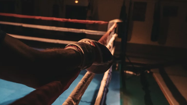 A close-up of a person’s gloved hand gripping the ropes, an intense scene reminiscent of Andrew Tate’s gritty fighting days